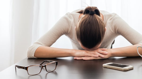 Exhausted woman with phone on desk - featured image
