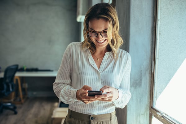 Smiling woman reading update on her phone from the office